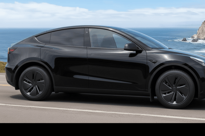 A red Tesla Model Y SUV parked on a coastal road with the ocean and rocky cliffs visible in the background.