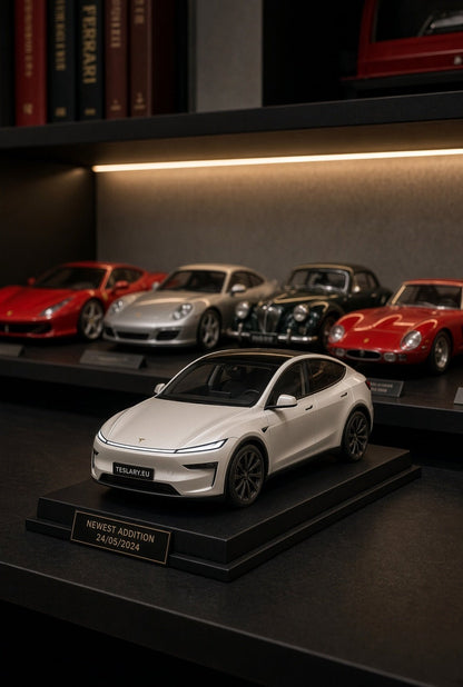 A white Tesla Model Y model car displayed on a black pedestal with a gold plaque, set on a dark shelf alongside other miniature classic cars under warm lighting. Tesla Model Y Juniper Childrens Scale Toy Collectors Edition Toy 1 32 Buy from Ireland and Europes Teslary.eu